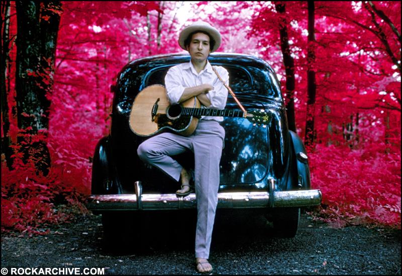 An 'infrared' colour print of Bob Dylan leaning against a car outside his Woodstock home in 1968.
