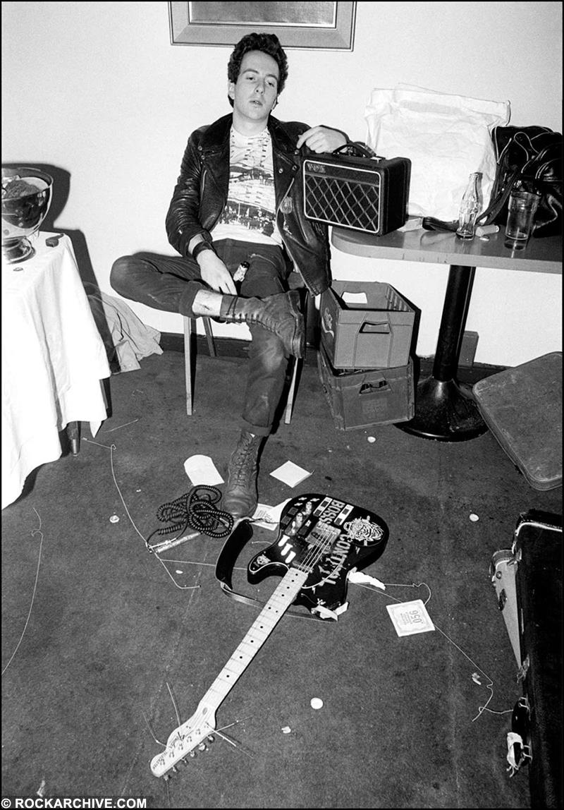 A limited edition Rockarchive print of The Clash's Joe Strummer sat in a room with guitar and amplifier.