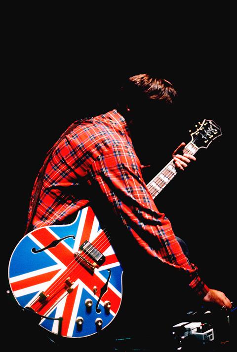 Noel Gallagher holding his iconic Union Jack Epiphone guitar at the NEC in 1996 during Oasis's Knebworth rehearsals