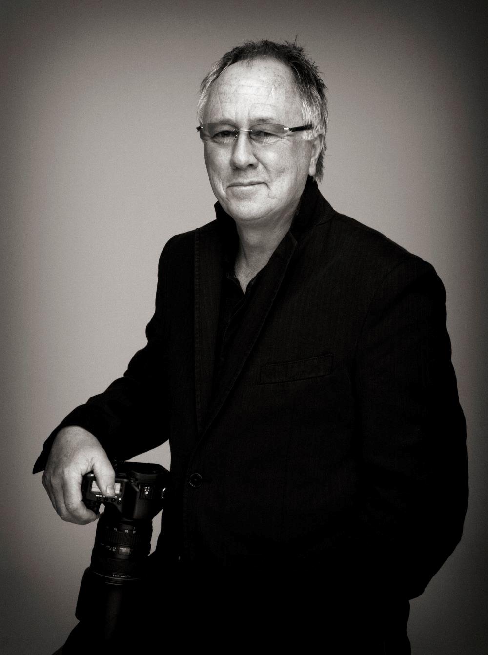 Photographer Brian Aris smiling whilst holding his camera.