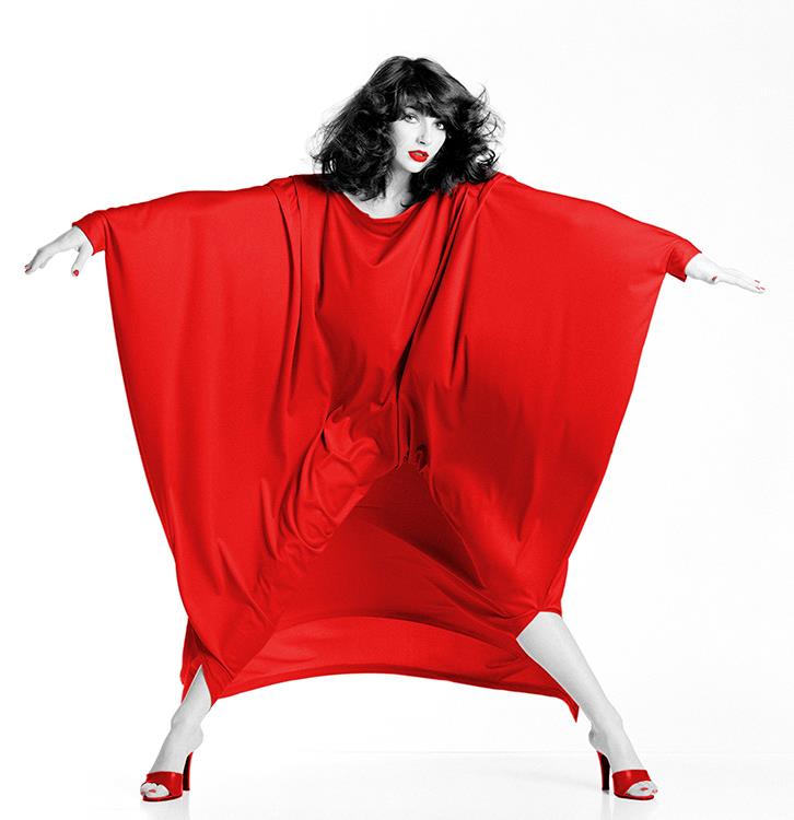 Kate Bush wearing a red dress that is being blown into shapes by a wind machine