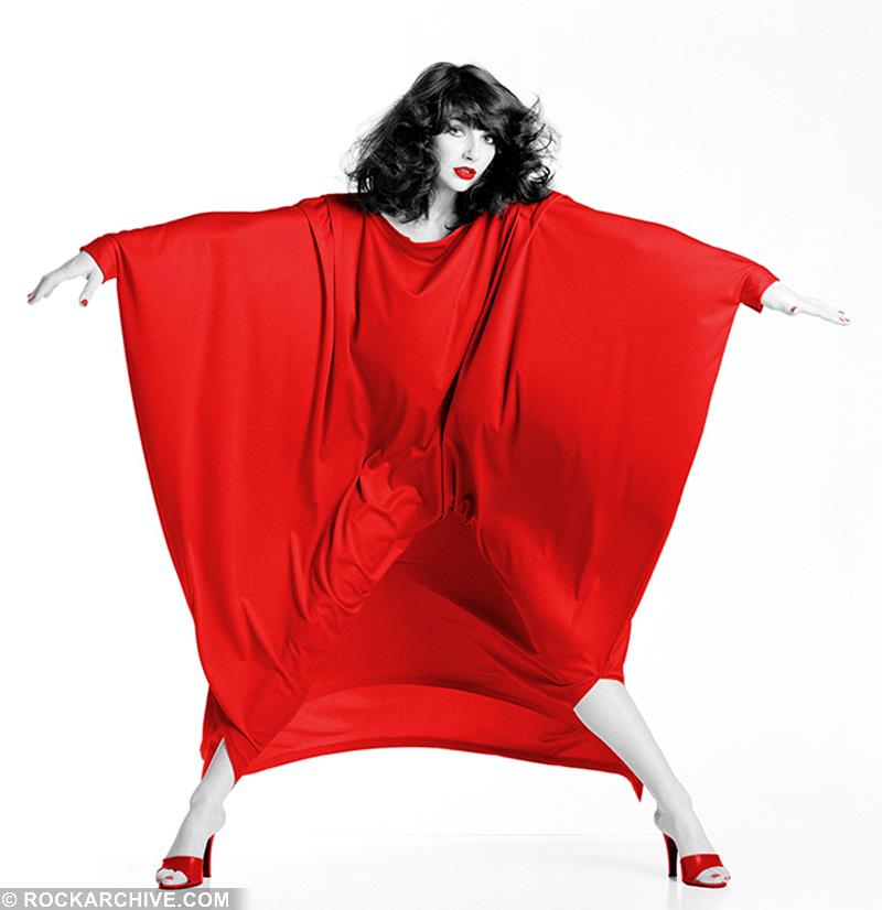 Kate Bush wearing a red dress that is being blown into shapes by a wind machine