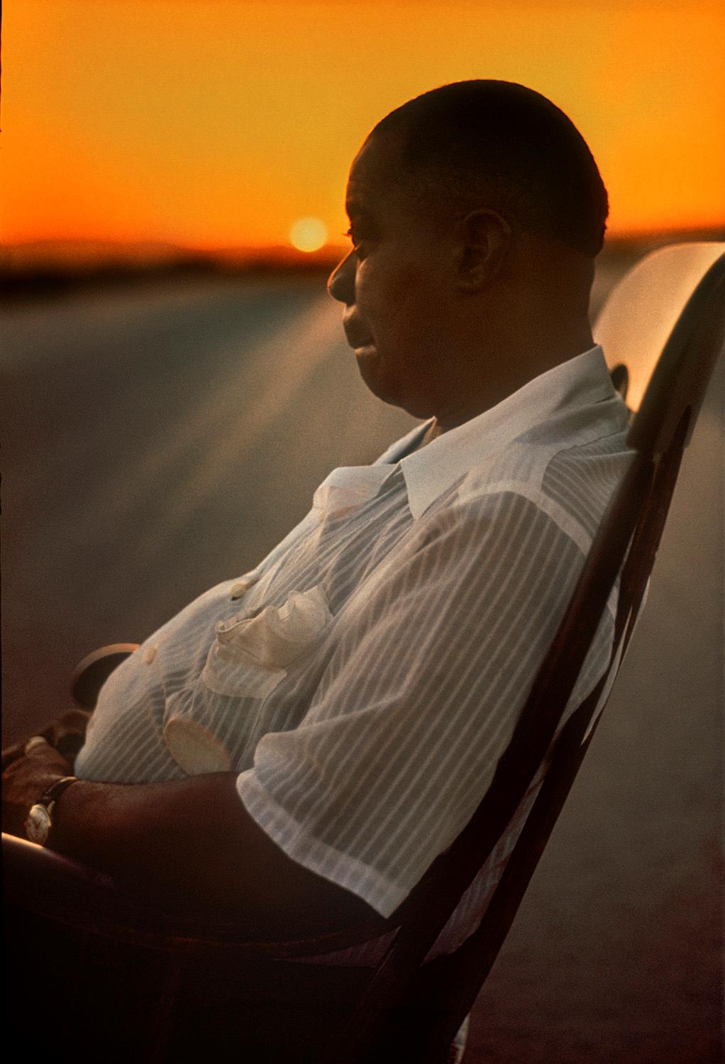 Louis Armstrong sat in a rocking chair with an orange sunset in the background