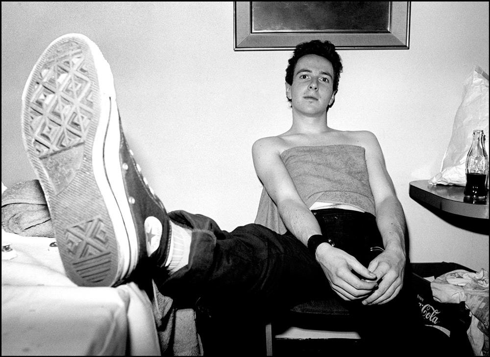 A limited edition Rockarchive print of The Clash's Joe Strummer sat on chair with his foot out.