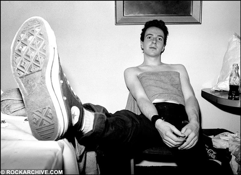 A limited edition Rockarchive print of The Clash's Joe Strummer sat on chair with his foot out.