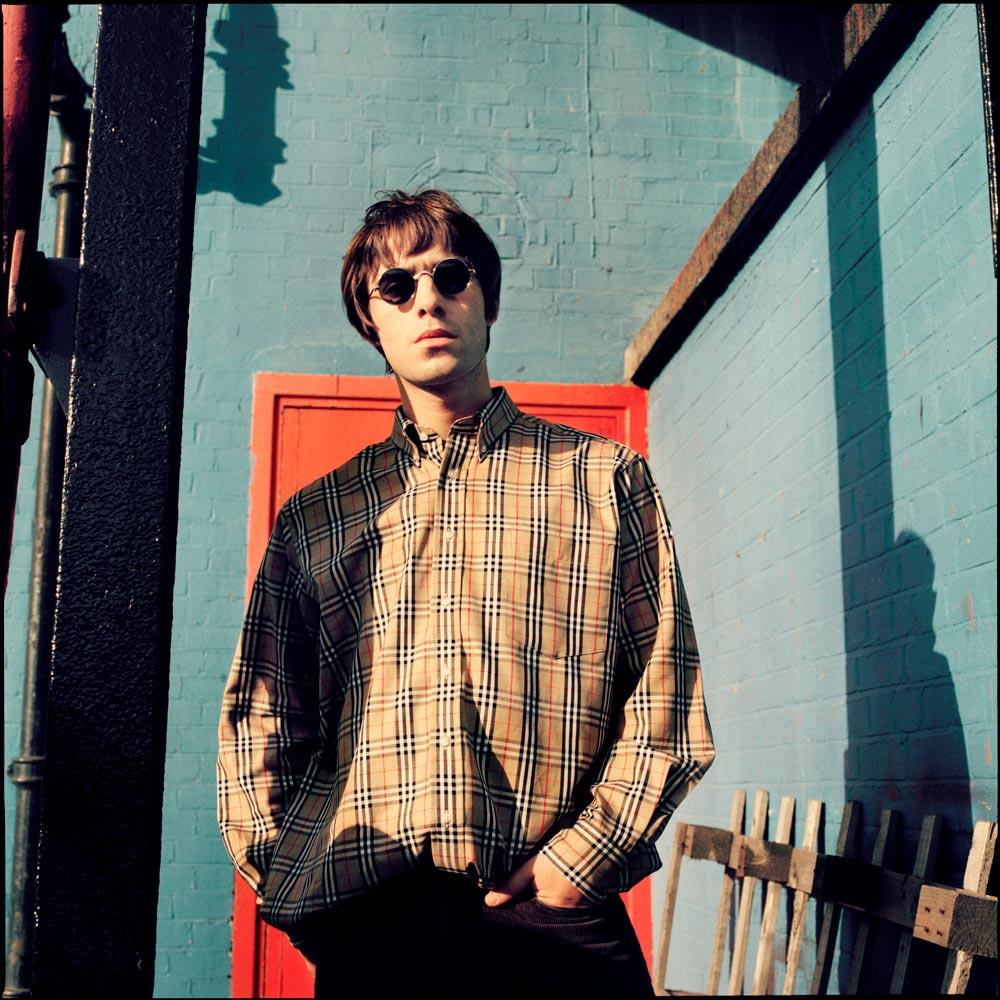 A limited edition Rockarchive print of Liam Gallagher stood by a wall wearing a Burberry shirt.