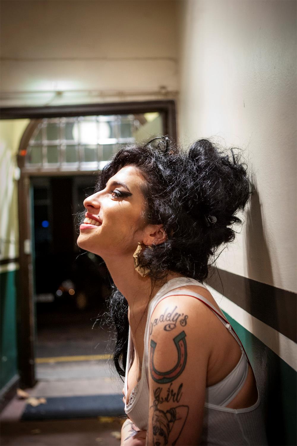 A limited edition colour print of Amy Winehouse from the side sitting and smiling.