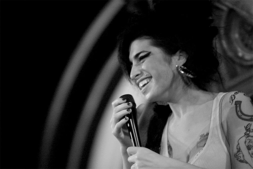 A limited edition print of Amy Winehouse from the side holding a microphone and smiling.