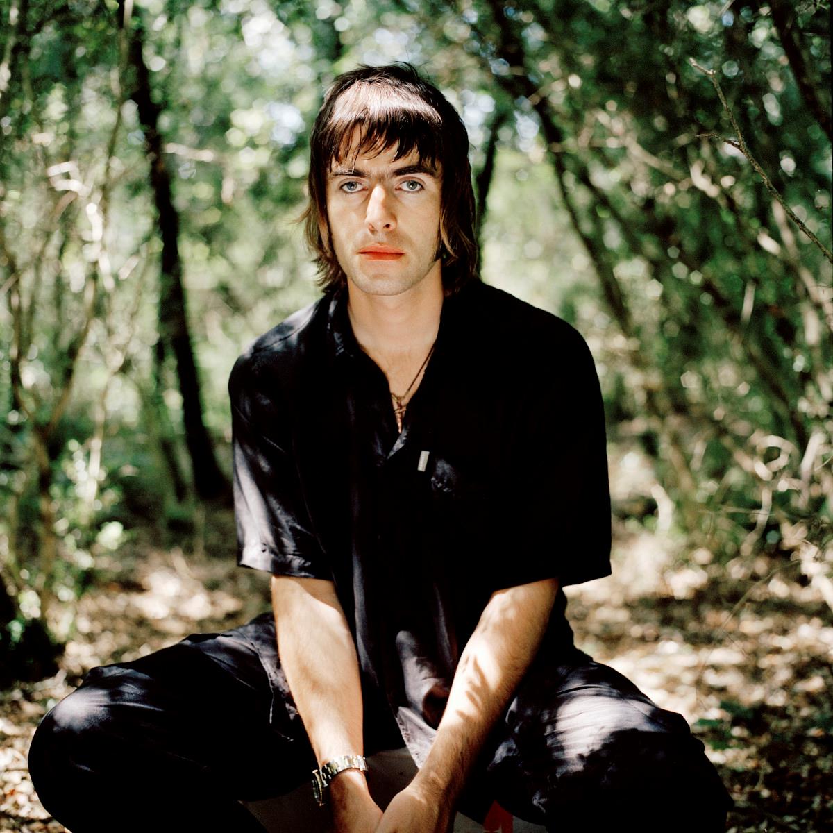 A limited edition colour print of Liam Gallagher sitting in nature looking at the camera.